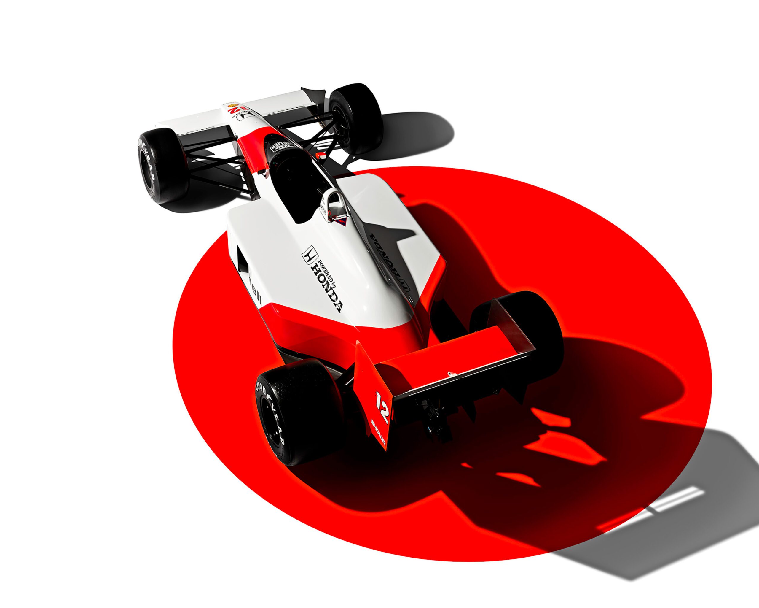 0050_807_WH_McLarenMP44_HighRear34_v2a Aerial view of a white and red Formula 1 race car, reminiscent of Ayrton Senna’s McLaren MP44, with the classic Honda logo on the side. Positioned against a white background with a large red circle beneath it, the car casts a shadow, adding depth through luxury retouching.