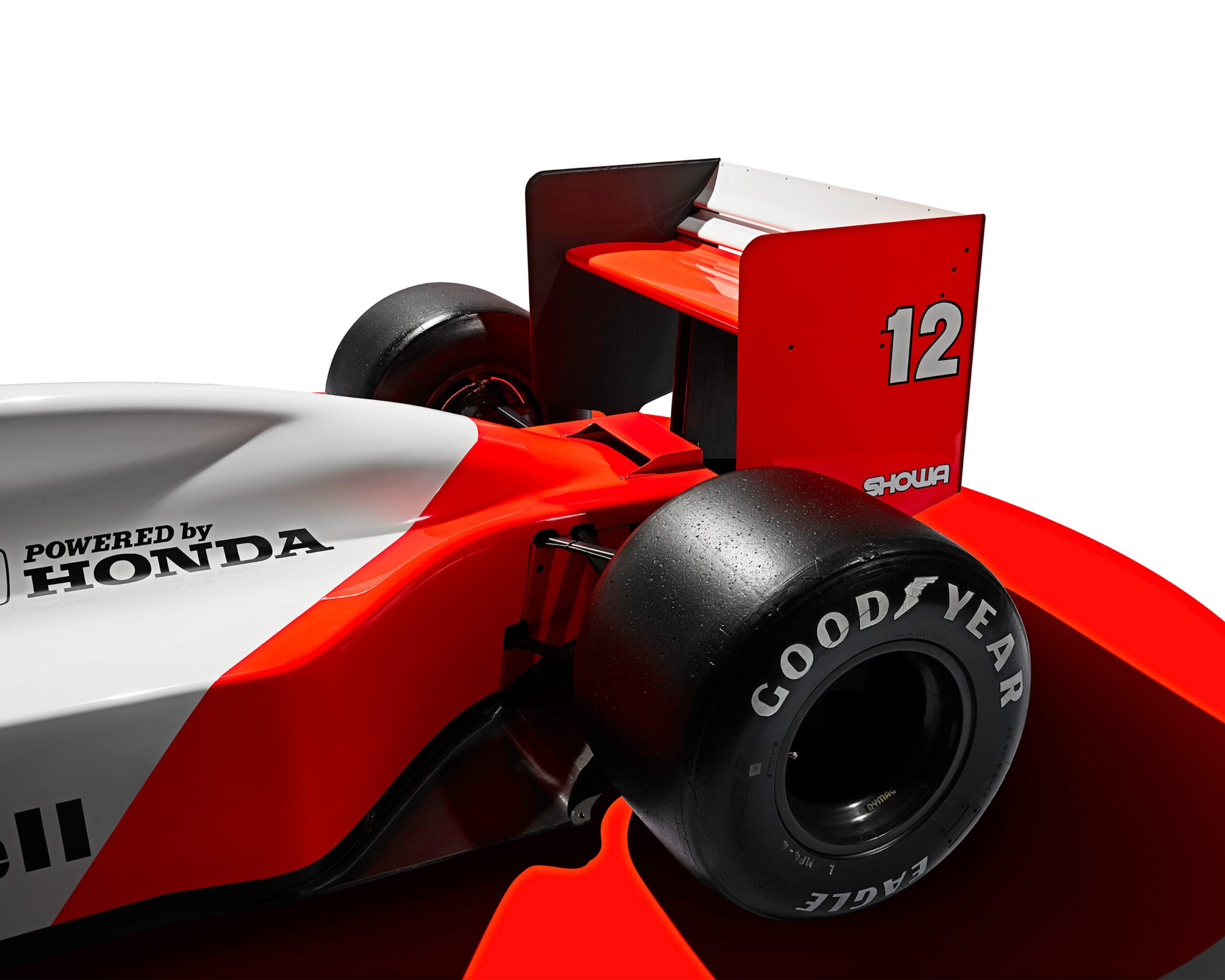 0050_807_WH_McLarenMP44_RrEnd_v3a Close-up of Ayrton Senna's McLaren MP44 race car's rear section, featuring prominent Goodyear tire branding, a large rear wing with the number 12, and a "Powered by Honda" logo on the side. The car is primarily red and white, with bold aerodynamic design elements benefiting from luxury retouching.