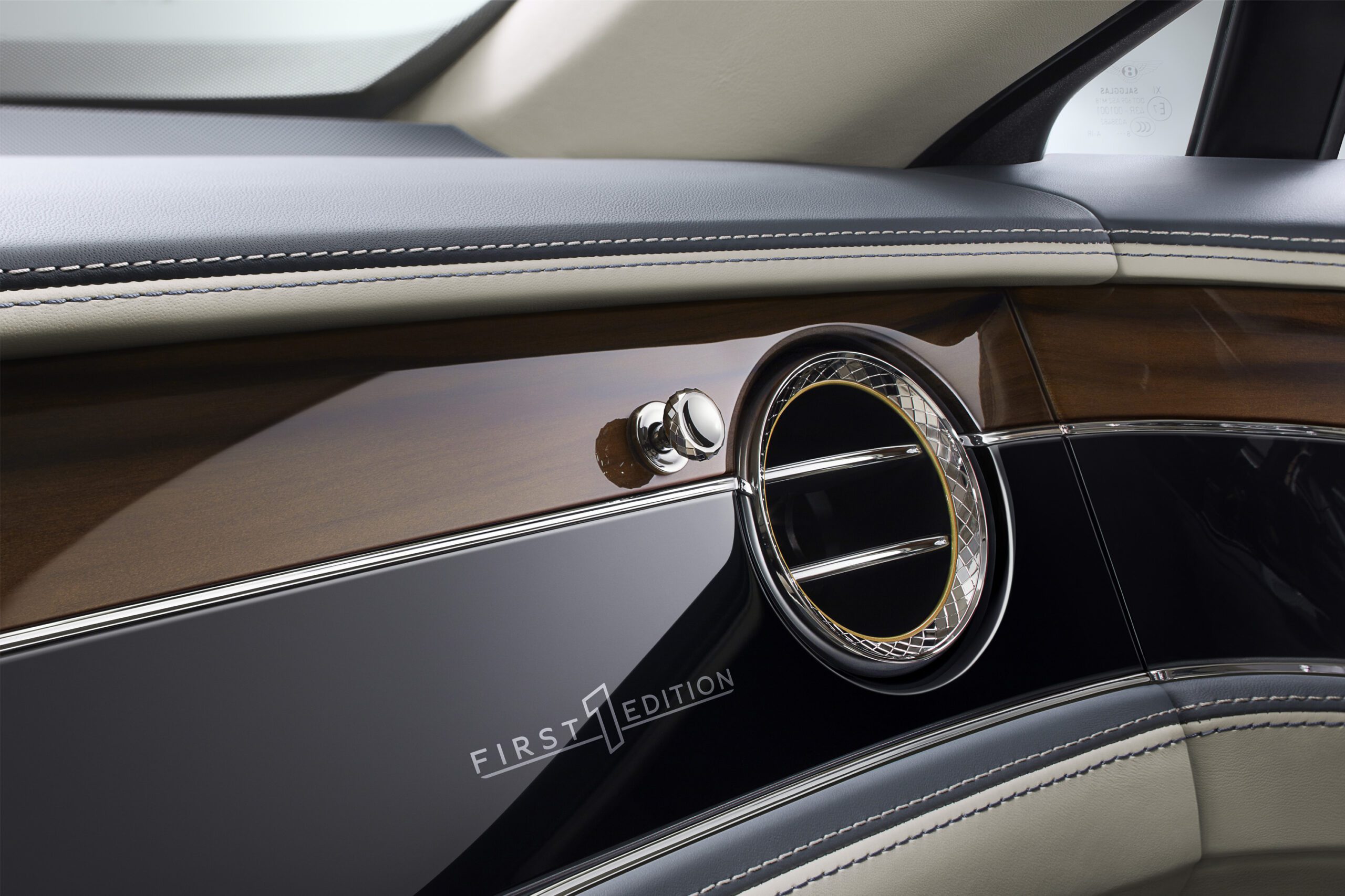 Close-up of a Bentley Flying Spur 2022's interior showcasing a sleek, luxurious design. The image features a wooden and leather dashboard with a circular air vent framed in chrome and a small "First Edition" emblem. The stitching on the leather is detailed and precise, perfectly highlighted by the car retoucher.