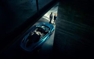 mclaren 720 spyder above right Elevated view of the McLaren 720S Spyder with a man and a woman standing beside it in a car park stairwell.