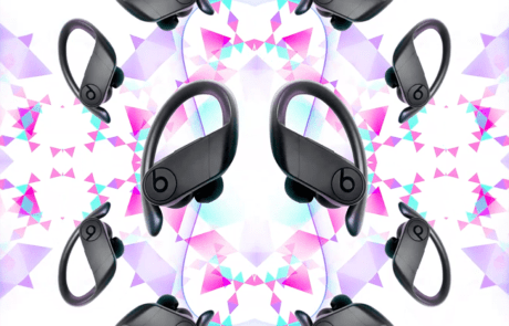 A symmetrical pattern with wireless earbuds. Eight pairs of black Beats headphones with over-ear hooks are arranged in a kaleidoscopic design. The background features an abstract geometric pattern with triangles in shades of pink, purple, and white, resembling the logo from Three network.