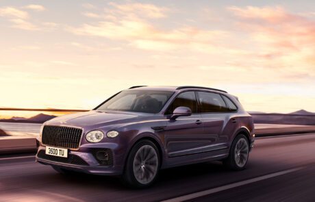 A CGI depiction of a purple Bentley Bentayga Extended Wheelbase SUV drives on a highway at sunset, set against a scenic background of mountains and a colorful sky. The vehicle boasts sleek design features, including a distinct front grille and modern headlights, with license plate "3500 TU" visible.