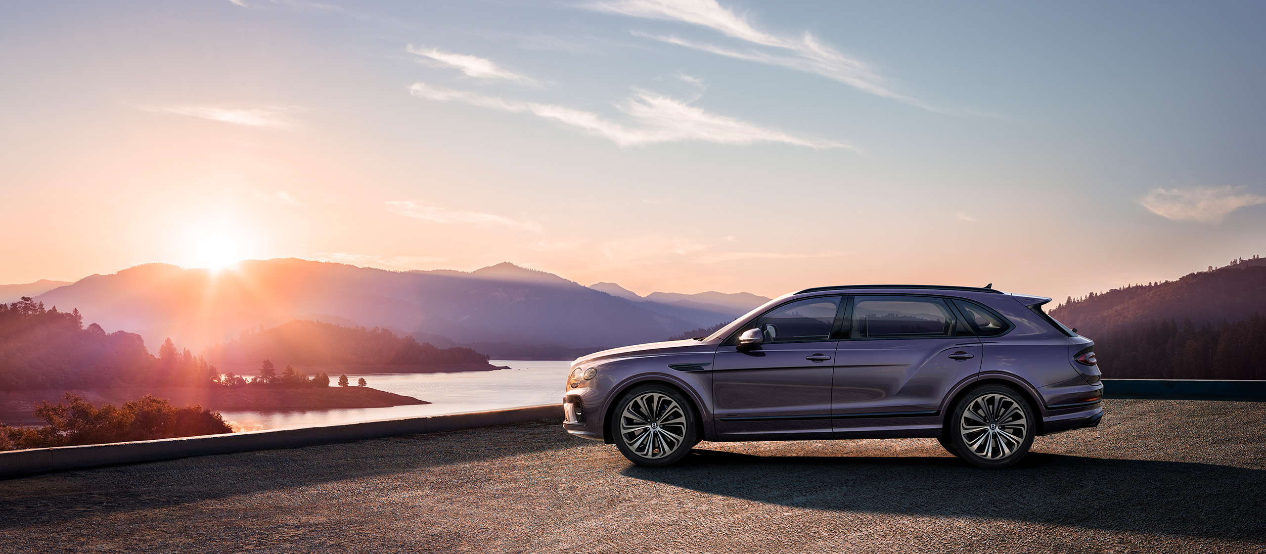 A sleek, CGI-rendered Bentley Bentayga Extended Wheelbase in a stunning purple hue is parked at an elevated viewpoint, overlooking a serene lake and mountain range at sunset. The sky is painted with delicate clouds and warm hues as the sun sets behind the mountains, casting a tranquil glow across the landscape.