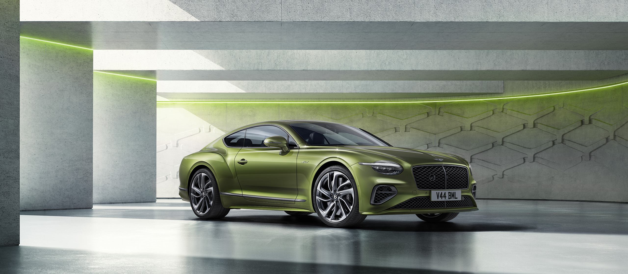 A green luxury sports coupe with sleek lines is parked in a modern, minimalist concrete garage with geometric wall patterns and subtle green accent lighting.