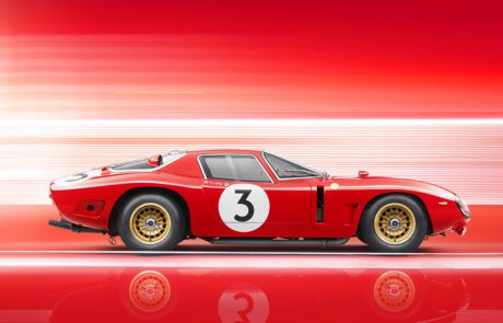 Side view of a sleek, red vintage Bizzarrini 5300 GT Corsa with the number 3 on its door and hood, set against a dynamic red and white blurred background. The car has gold rims and an aerodynamic design, creating a sense of speed and motion in this retouched image.