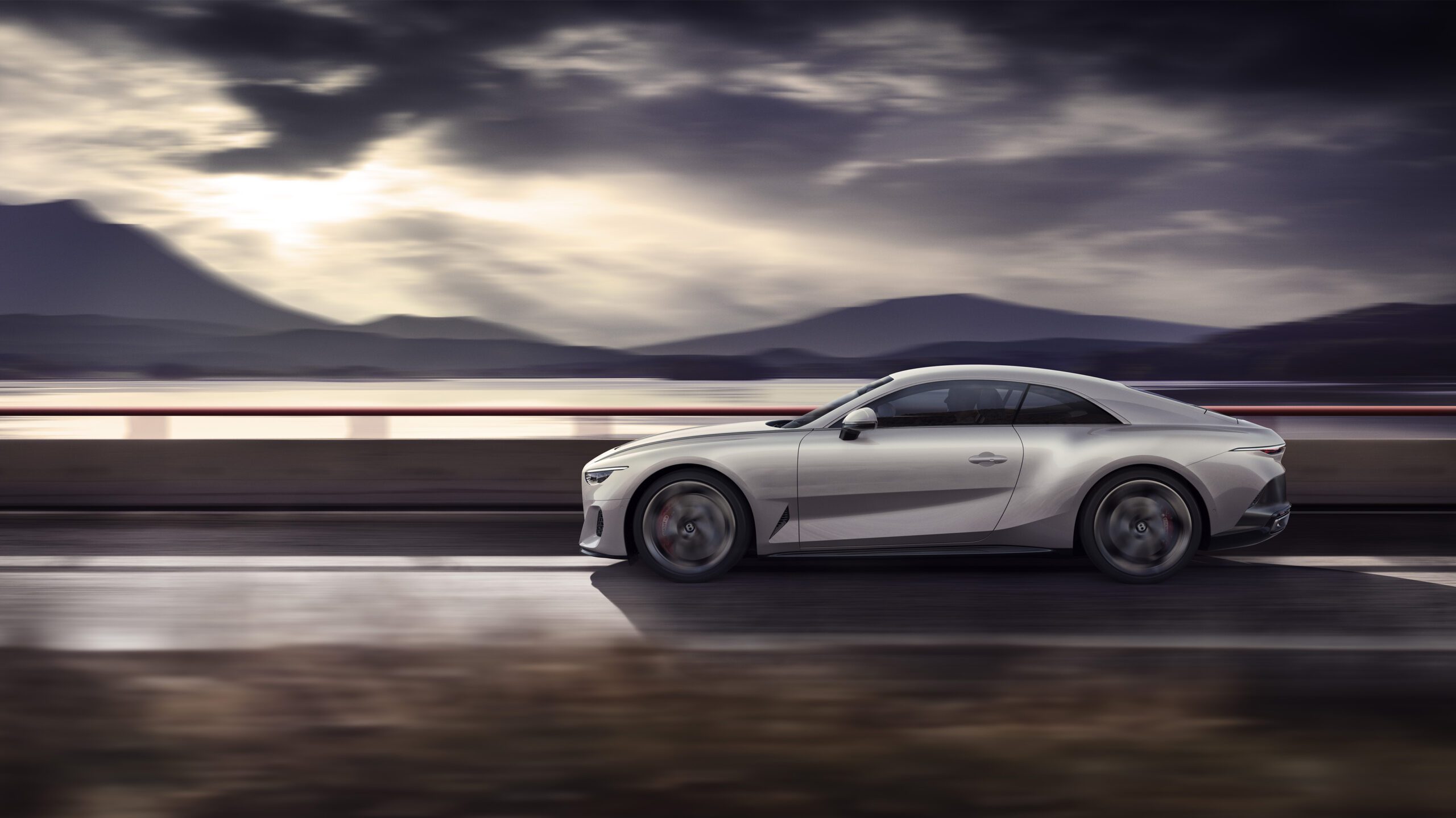 A sleek silver Bentley Batur hypercar is driving on a road with a mountainous landscape in the background. The sky is cloudy, casting a dramatic light over the scene. The car, rendered immaculately by a CGI artist, is moving fast, creating a sense of motion and speed.