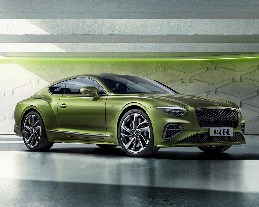 A sleek, green, two-door sports car is parked in a modern, industrial setting. The car features a black roof, silver alloy wheels, and a distinctive grille with a "V44 BML" license plate. The background includes geometric wall designs and neon green lighting.