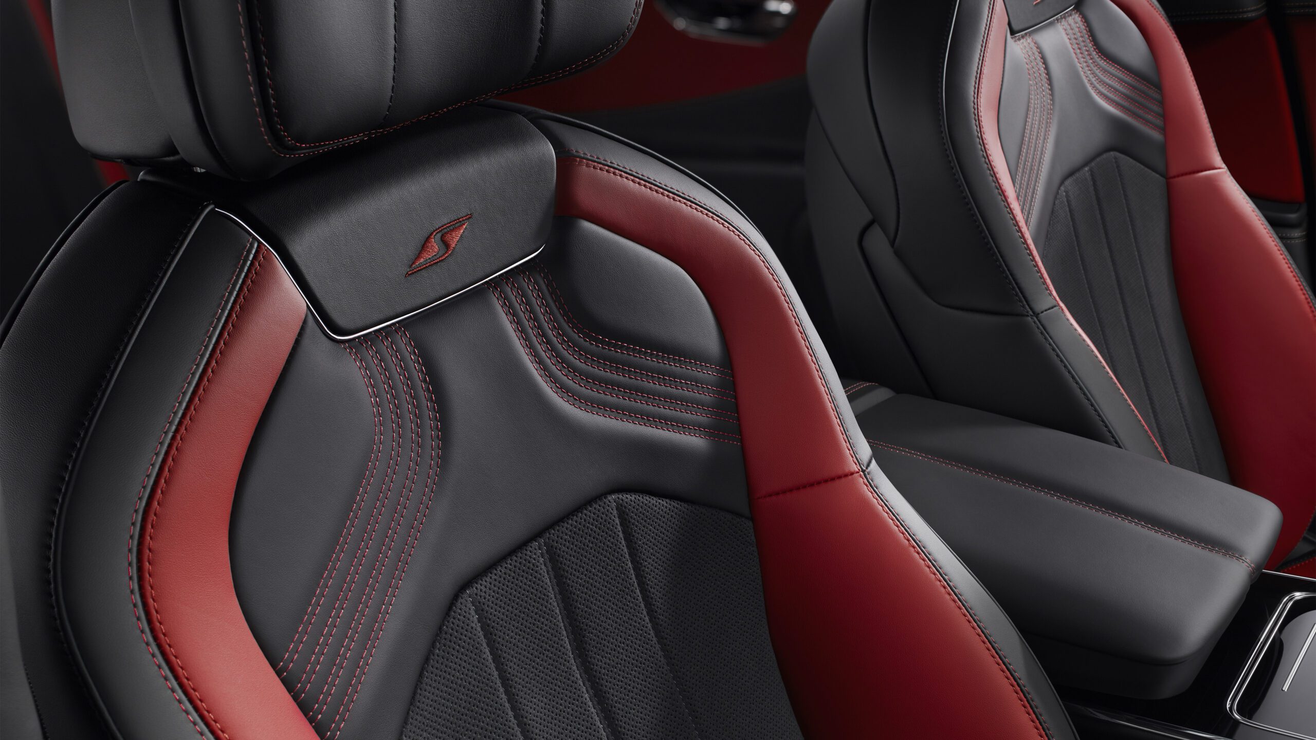 Close-up of the front seats of a Bentley Flying Spur S, featuring black and red leather upholstery with retouched, detailed stitching. The seats are stylishly contoured and include headrests and armrests for added comfort.