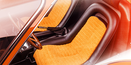 The image shows the interior of a vintage Ferrari Dino, featuring seats upholstered in bright orange fabric with black trim. The steering wheel and gear shift are also visible, with light shining in from the top left corner. This stunning was retouched by professionals like those at Mustard Post.