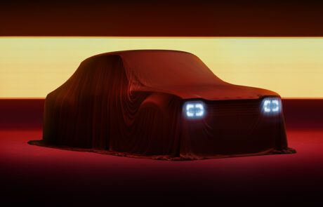 A car covered with a red sheet is illuminated by its headlights, creating a dramatic effect. The background is dark with a horizontal band of yellow light, enhancing the mysterious and revealing atmosphere of the scene, perfect for an automotive retoucher to capture the essence of a Ford Escort Mk1 DRVN.