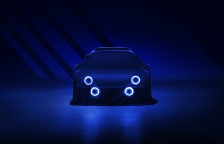 A dark and sleek image of a Ford RS2000 DRVN draped in a cloth, partially illuminated by four glowing circular lights on its front. The overall scene is bathed in deep blue tones, giving a futuristic and mysterious ambiance reminiscent of a car retoucher’s meticulous work.