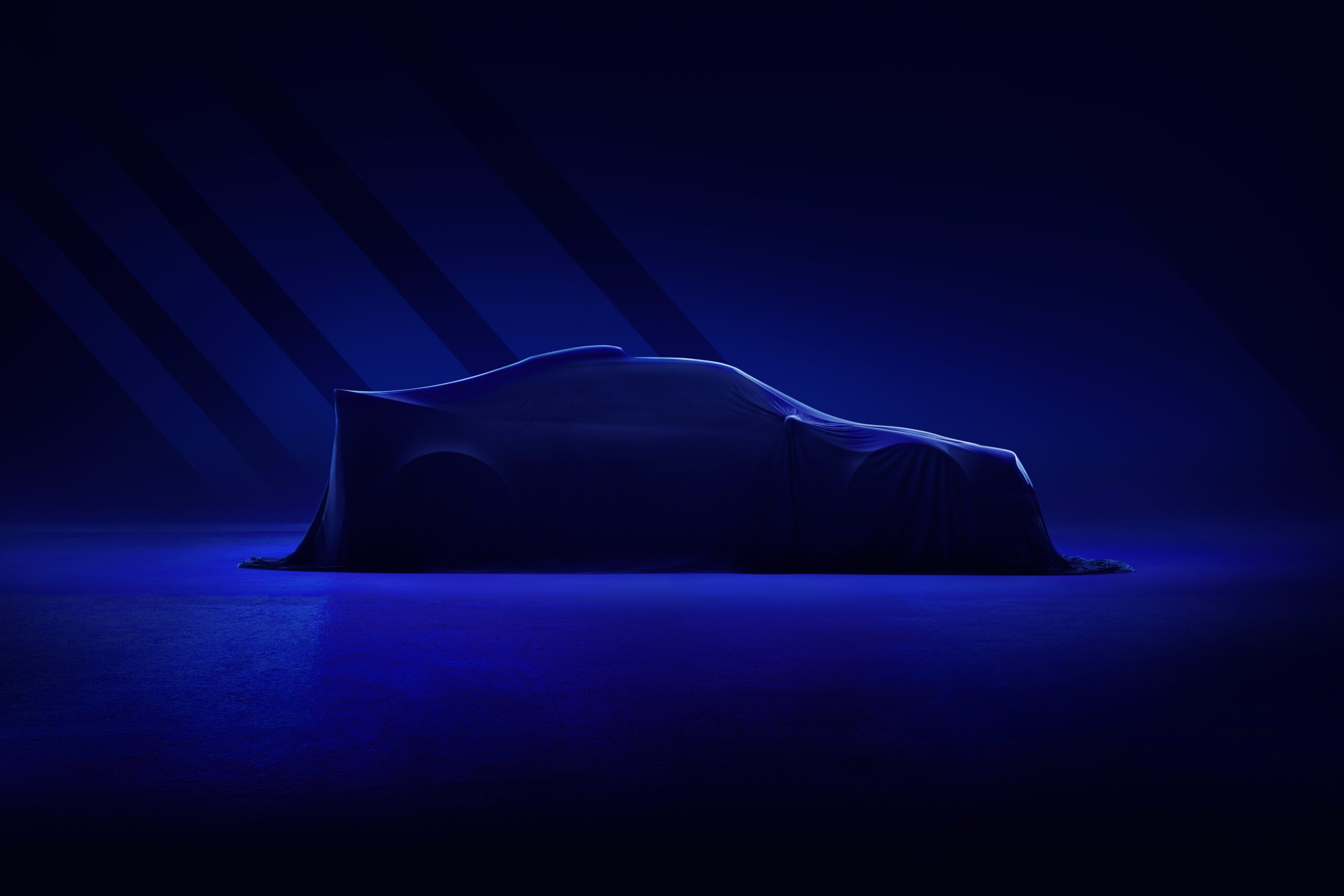 A Ford RS2000 DRVN is draped in a dark fabric cover in a dimly lit room with blue lighting. The outline of the car's sleek, aerodynamic shape is visible under the cover, suggesting a sense of mystery and anticipation. The background is dark with light casting geometric shadows, all masterfully enhanced by a car retoucher.