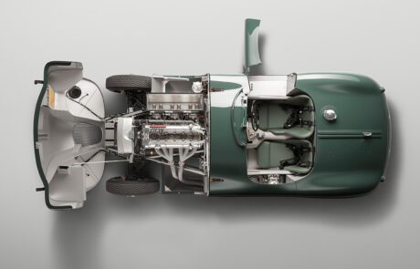 Top-down view of a classic green Jaguar C-Type with the hood open, revealing the detailed engine and mechanical components. The interior features two seats, a steering wheel on the right, and a minimalistic design, beautifully captured by a high-end retoucher.