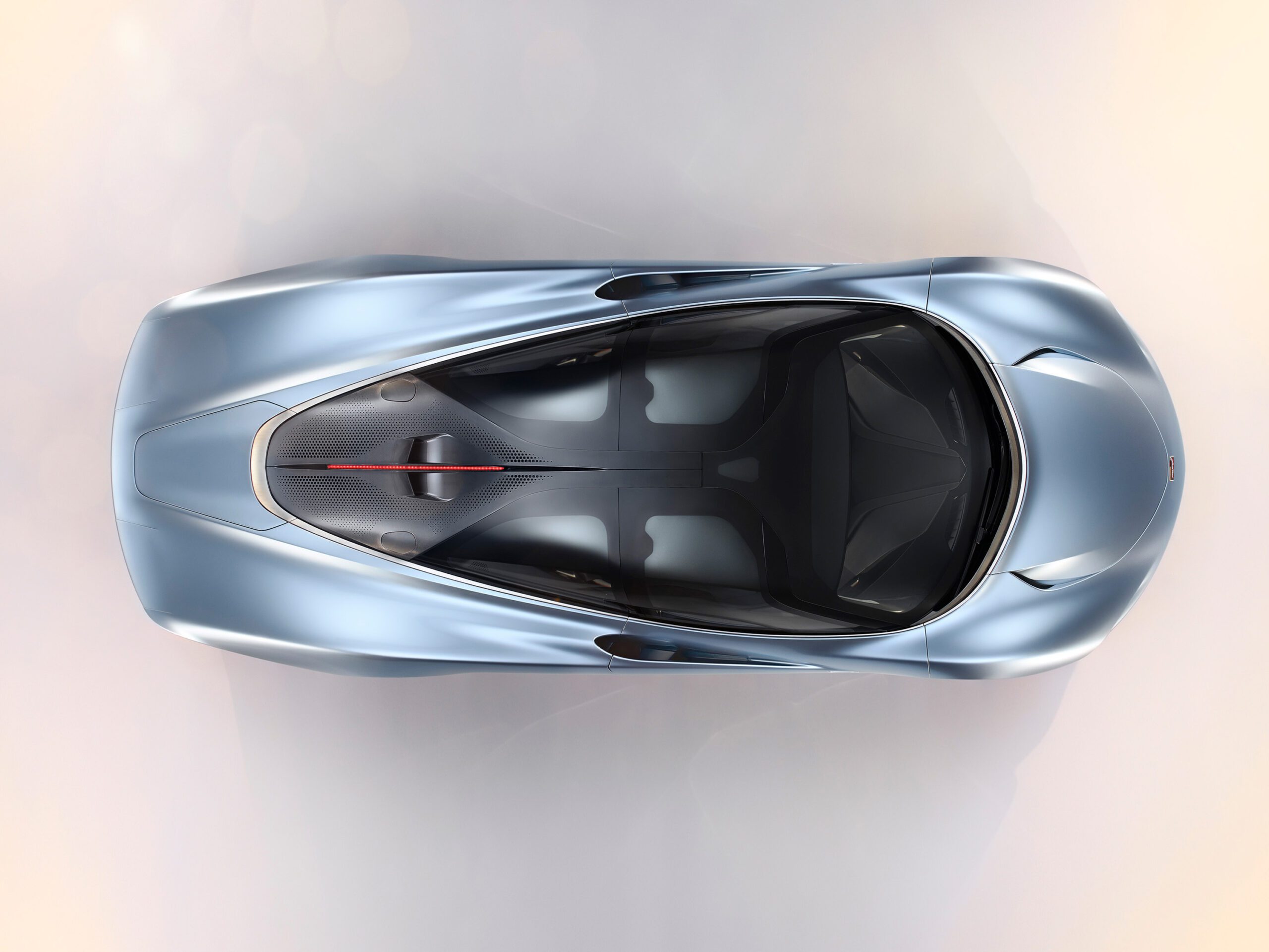 A top-down view of a sleek, modern, metallic silver-blue McLaren Speedtail. The design features smooth, aerodynamic lines and has a low, elongated body. Sunlight highlights the car's contours, giving it a polished finish that any car retoucher would admire.