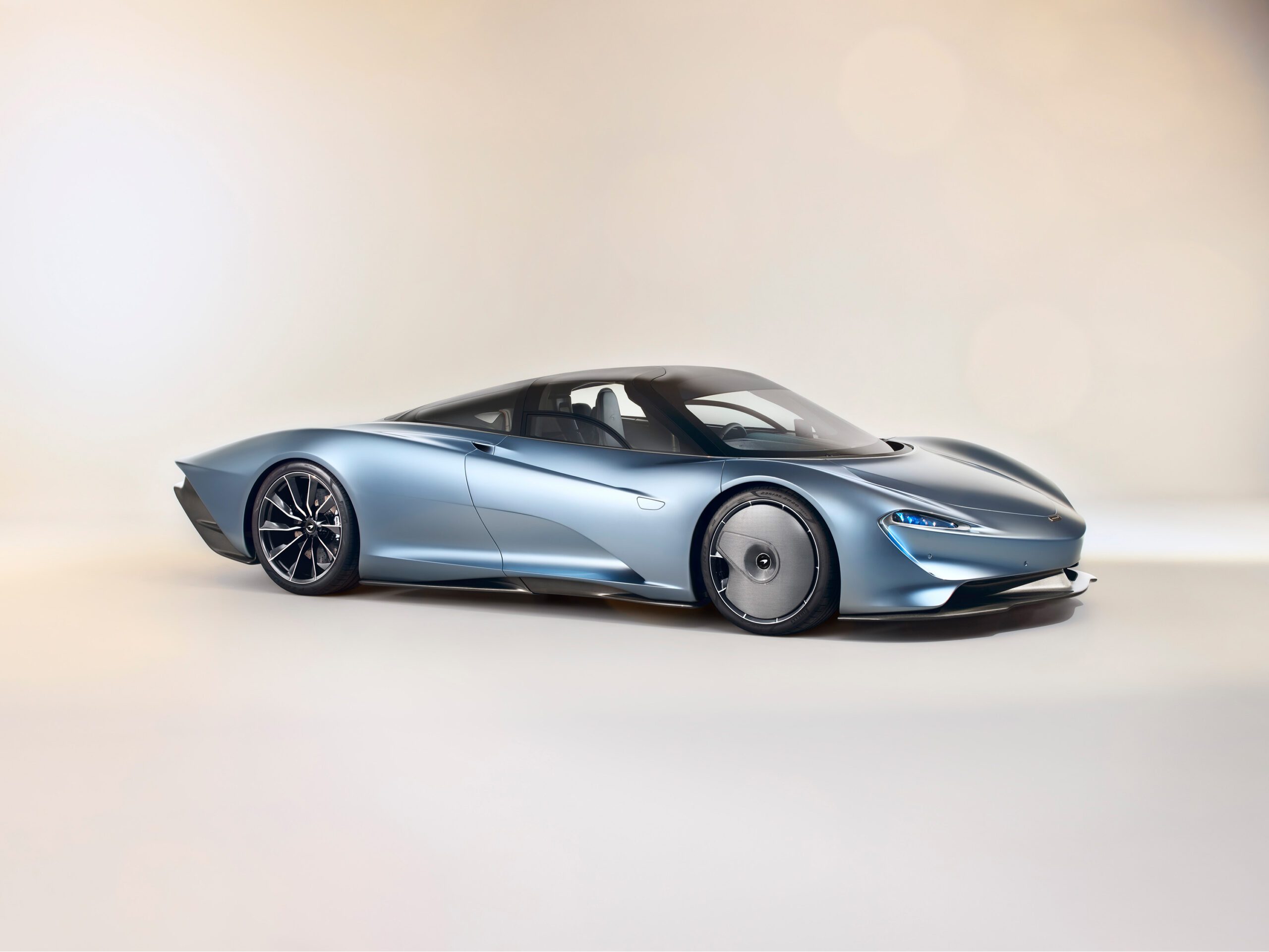 A sleek, futuristic silver-blue McLaren Speedtail with an aerodynamic design is displayed on a neutral background. The car features a low profile, smooth curves, dark tinted windows, and unique wheels, emphasizing its modern and high-performance characteristics. Perfect work by a skilled car retoucher.