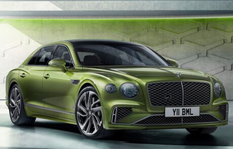 A sleek, green luxury Bentley Flying Spur Speed with a modern design is shown parked indoors. It features a distinctive mesh grille and stylish alloy wheels. The license plate reads "Y11 BML." The background has a CGI-inspired futuristic look with green lighting and geometric shapes on the walls.
