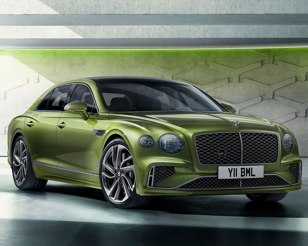 A sleek, green luxury Bentley Flying Spur Speed with a modern design is shown parked indoors. It features a distinctive mesh grille and stylish alloy wheels. The license plate reads "Y11 BML." The background has a CGI-inspired futuristic look with green lighting and geometric shapes on the walls.