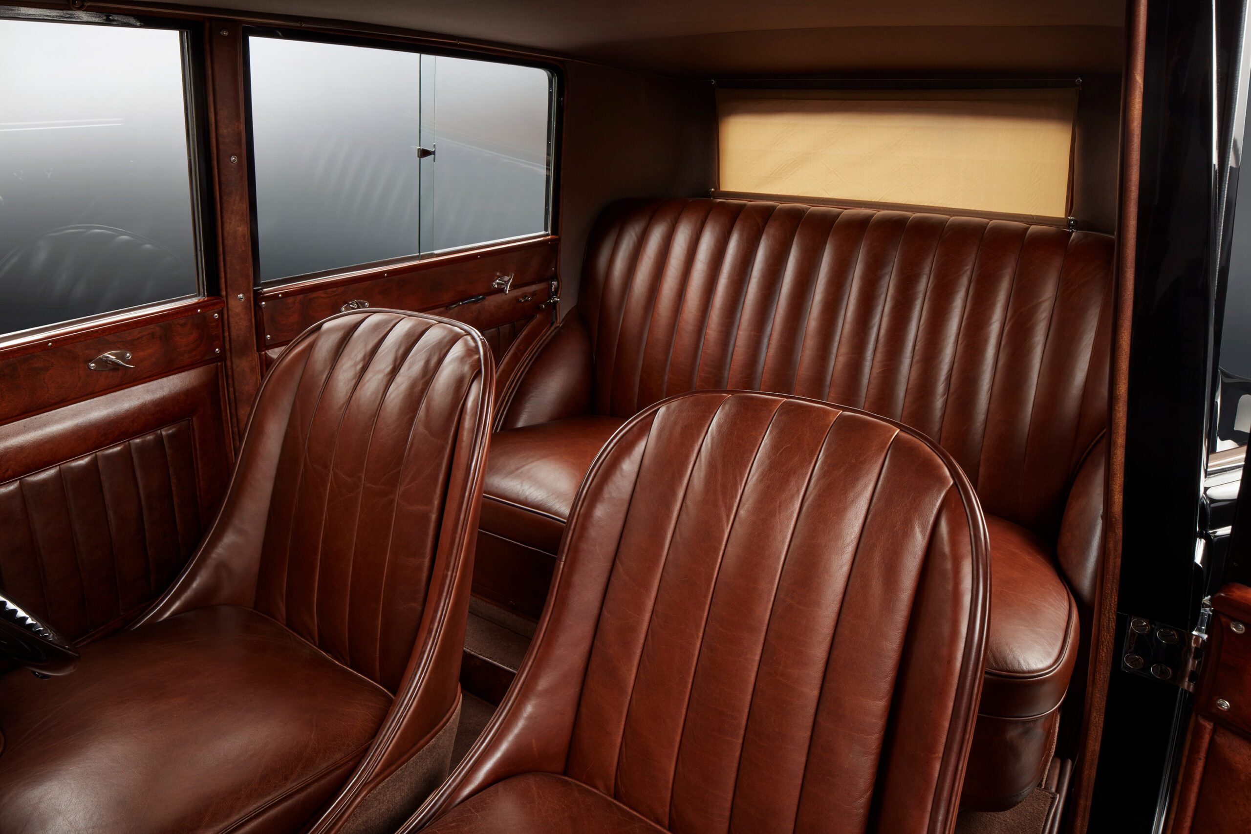 WO Bentley's own 8 litre car featuring luxurious brown leather seats with vertical stitching patterns. The front and back seats are spacious, showcasing elegant wood paneling on the doors and a partially visible window with a beige shade.