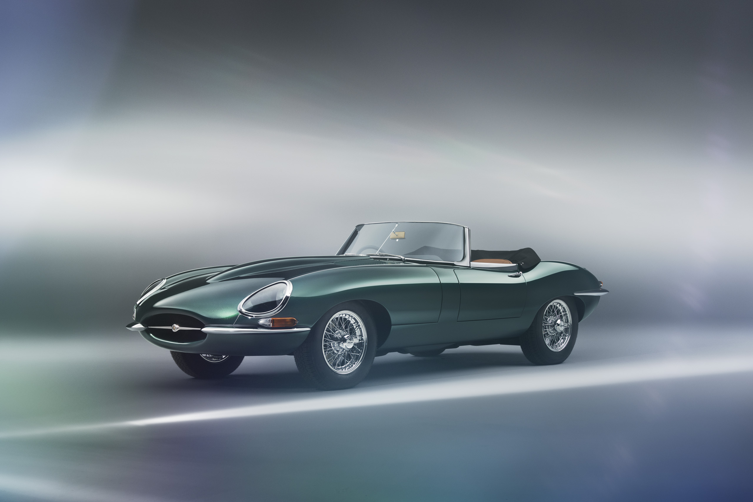 A classic green convertible sports car with a sleek, vintage design is displayed against a blurred, gradient background. The car features chrome accents, wire wheels, and an open-top, highlighting its elegant and timeless style.