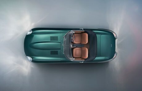 Aerial view of a classic green convertible car with brown leather interior. The car is positioned on a light, misty surface, emphasizing its sleek design and elegant lines.