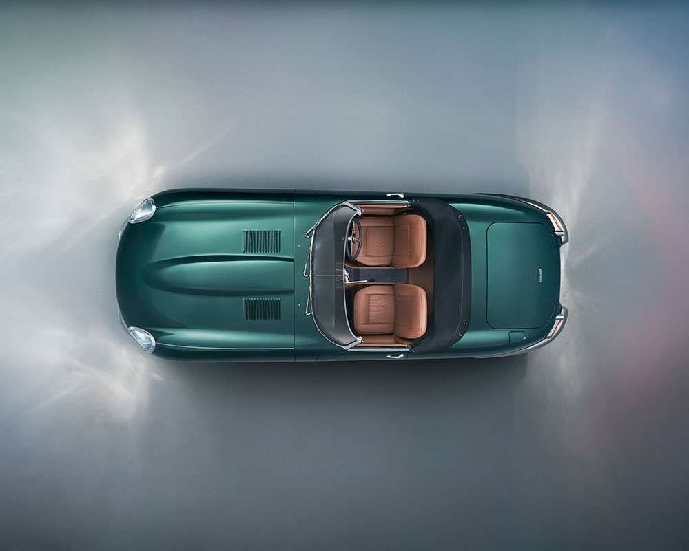 Aerial view of a classic green convertible car with brown leather interior. The car is positioned on a light, misty surface, emphasizing its sleek design and elegant lines.