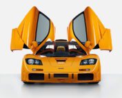 Front view of an orange sports car with its butterfly doors open, showcasing a sleek and aerodynamic design. The car is positioned against a plain white background.