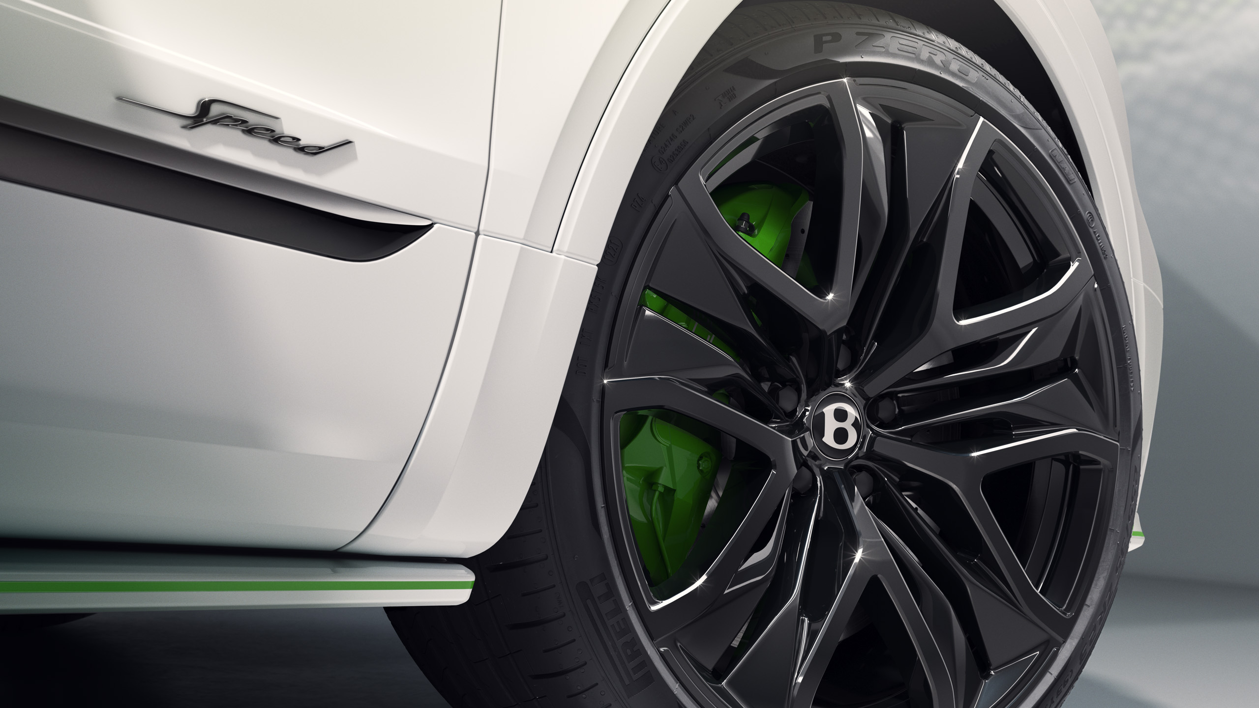 Close-up of a black Bentley wheel with green brake calipers on a white car. The “Speed” badge and Pirelli P Zero tire branding are visible, highlighting luxury and sporty design details.