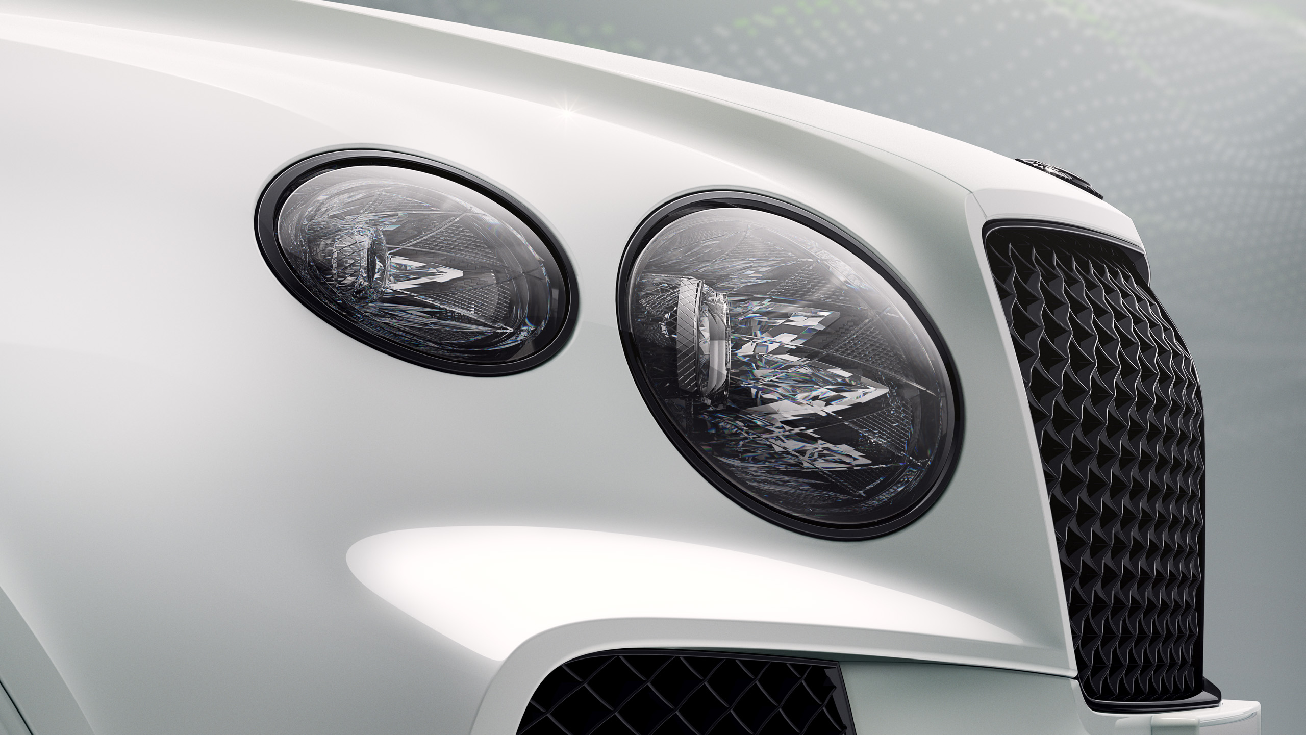 Close-up view of the front of a white luxury car, featuring two round, intricate headlights and a textured black grille. The background is softly blurred with light green and white tones.
