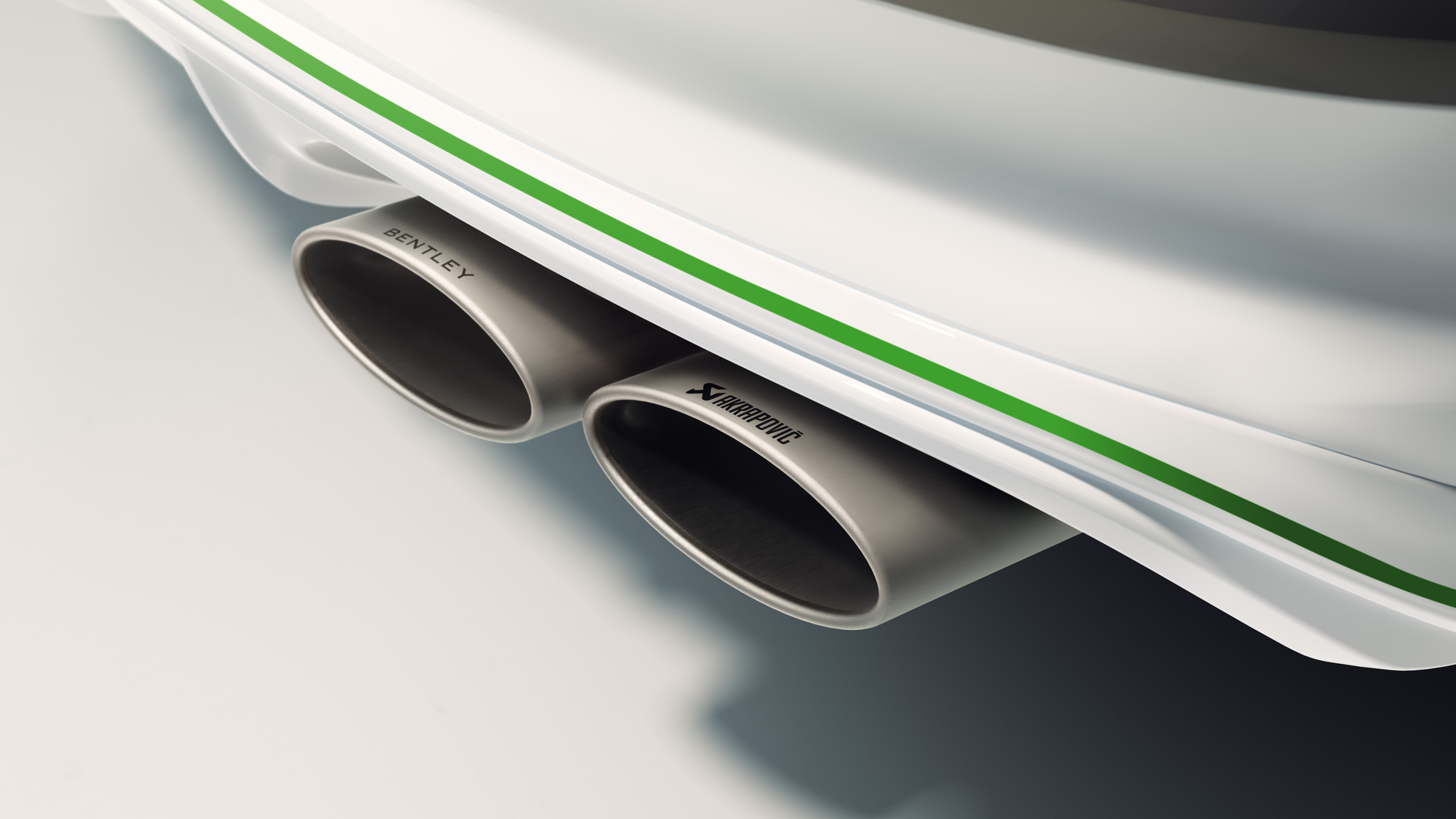 Close-up of twin metal exhaust pipes on a white Bentley car with green trim; the pipes are branded with “BENTLEY” and “Akrapovič.”.