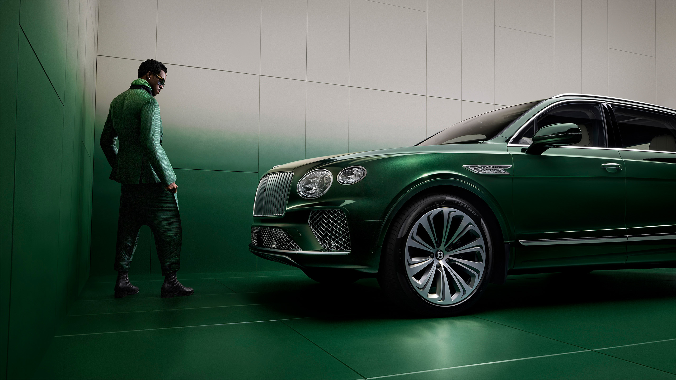 A stylish person in green clothing stands against a green wall, facing a luxurious green Bentley SUV parked indoors. The image has a modern, high-fashion aesthetic.