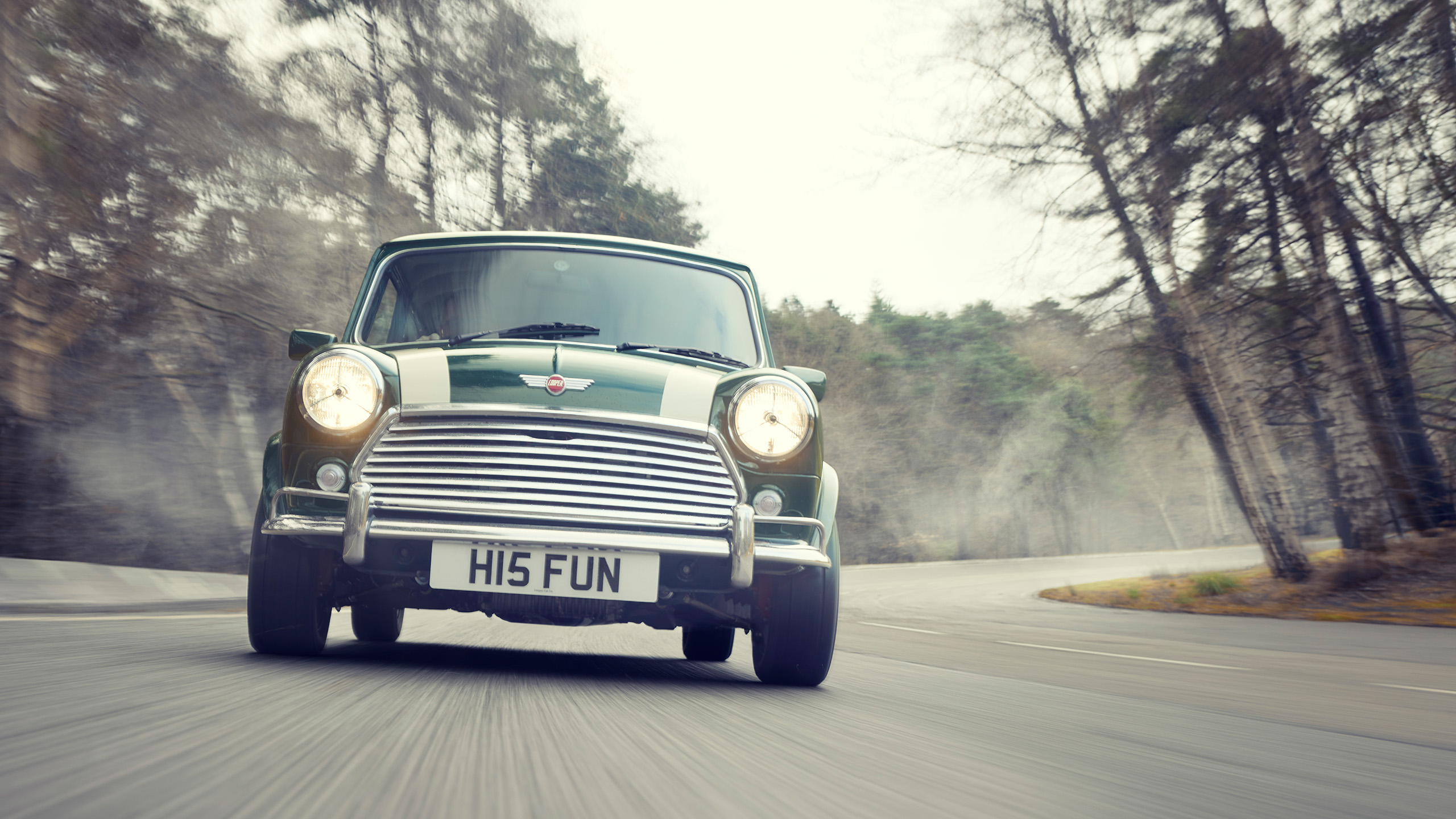 mini-cooper-grand-prix-cooper-cars-front-on-headlights Head-on view of the new Mini Cooper Grand Prix with headlights on, driving through a misty woodland road.