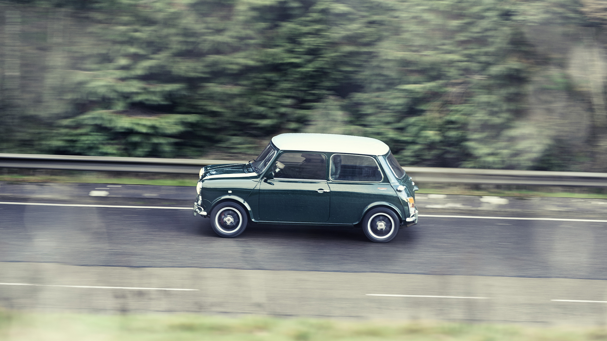mini-cooper-grand-prix-cooper-cars-side-profile-driving Side profile of a classic green and white Mini Cooper Grand Prix driving along a forest-lined road.