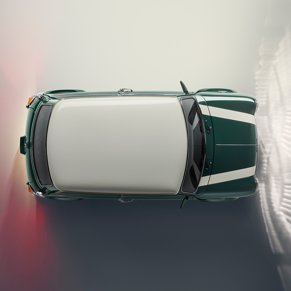 A top-down view of a green classic car with white racing stripes and a white roof, parked on a light-coloured surface with a gradient shadow to the side.