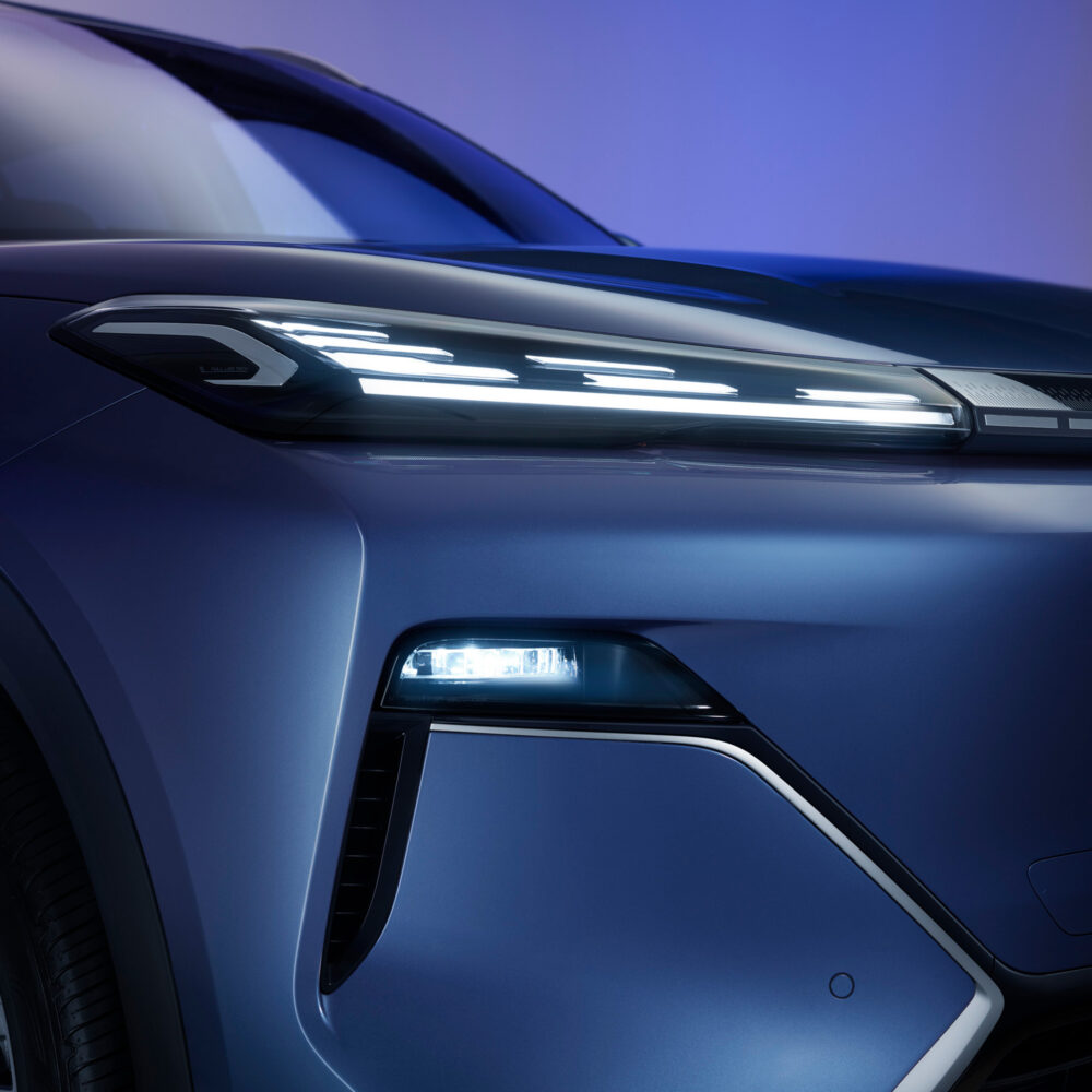 Close-up of a modern electric car’s front left headlamp and sleek blue body, with bright LED lights illuminated against a blue and purple gradient background.