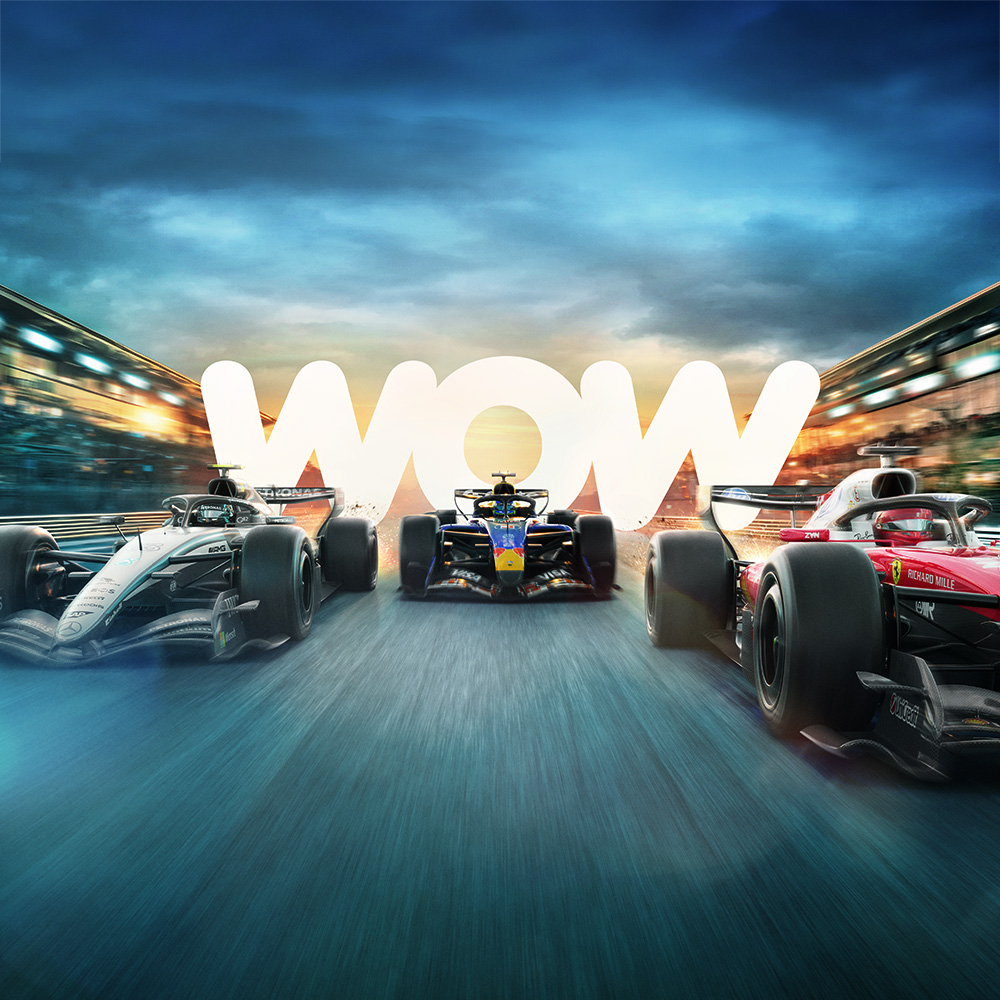 Three Formula 1 cars race side by side on a track at dusk, with glowing “WOW” text in the background, blurred stadium lights, and a dynamic sense of speed.