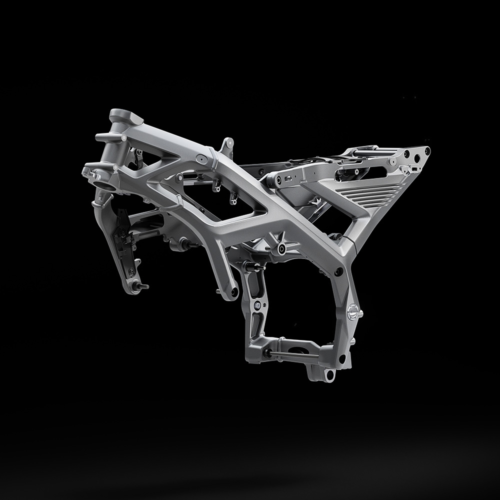 A metallic motorbike frame is suspended against a black background, showcasing its intricate structure and angular supports.
