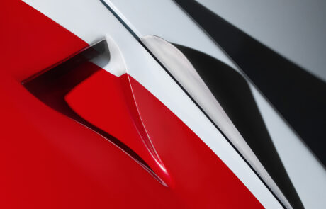 Close-up of a red, white, and grey abstract surface with sharp angles and shadows, possibly part of a car or vehicle bodywork, highlighting sleek, modern design.