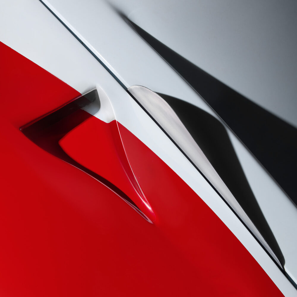 Close-up of a red, white, and grey abstract surface with sharp angles and shadows, possibly part of a car or vehicle bodywork, highlighting sleek, modern design.