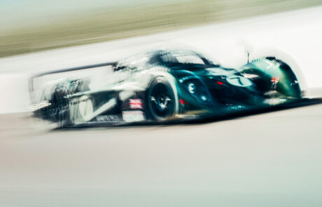 A green Bentley Speed 8 Le Mans prototype racing car cornering at speed, motion blur emphasising its curved bodywork and number 7 livery.