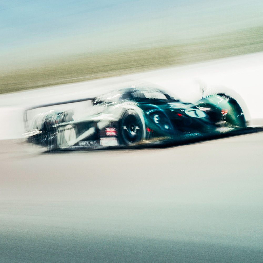 A green Bentley Speed 8 Le Mans prototype racing car cornering at speed, motion blur emphasising its curved bodywork and number 7 livery.