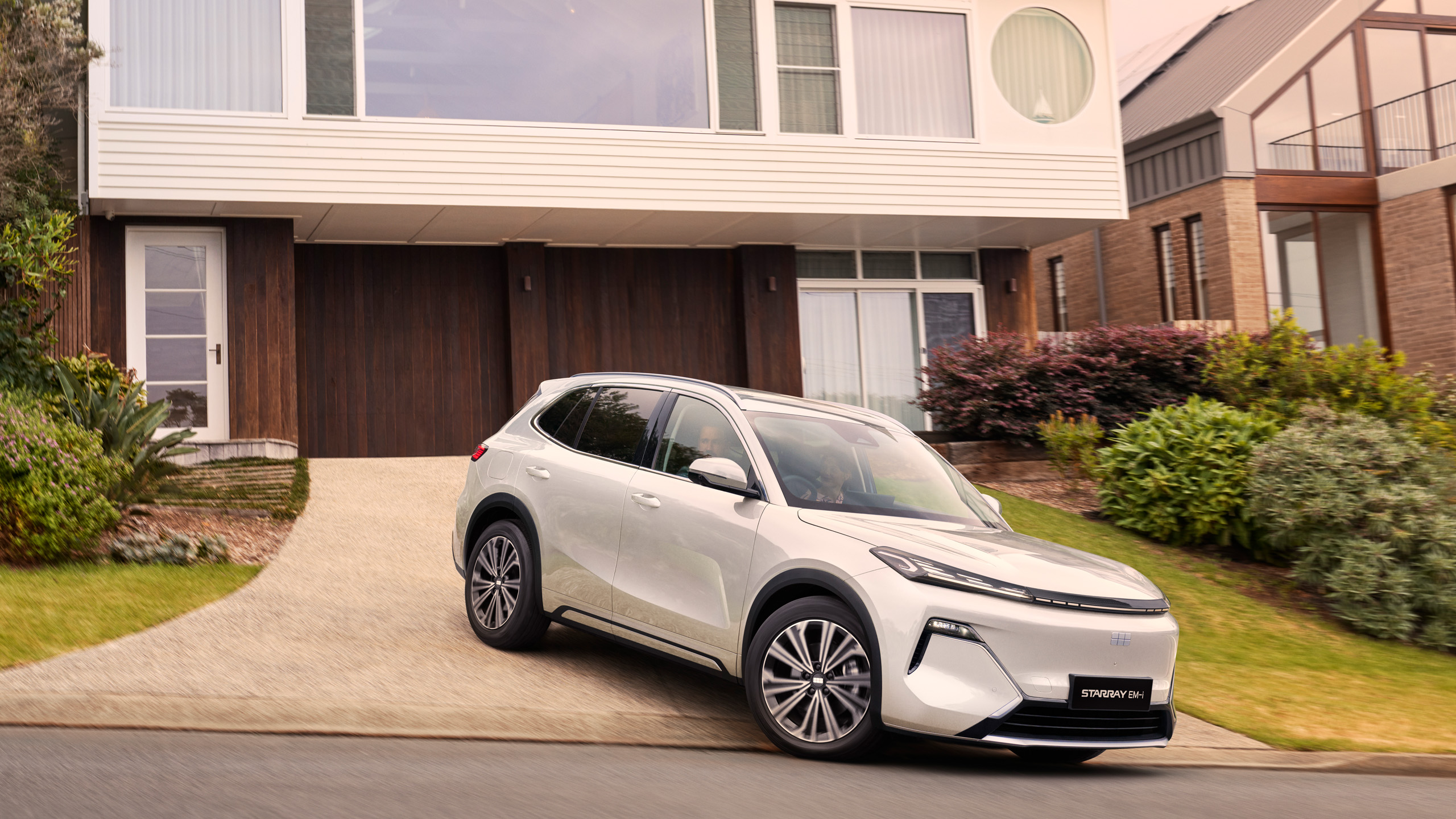 geely-starray-emi-driving-away-modern-house The Geely Starray EM-i drives away from a modern home, front three-quarter view.