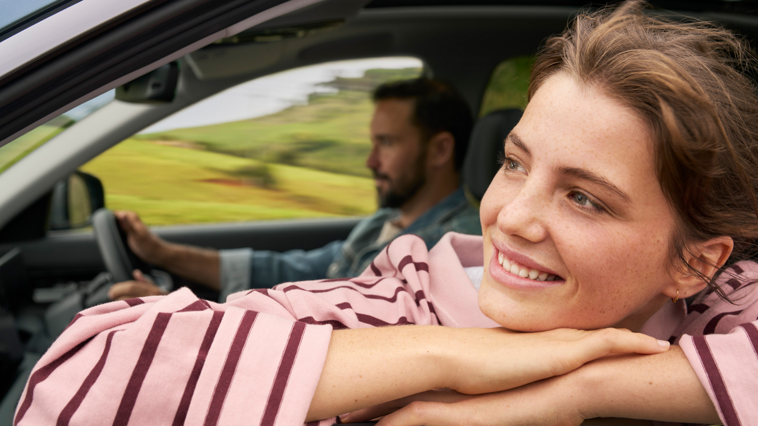 geely-starray-emi-driving-countryside-portrait A woman leans out of the passenger window of the Geely Starray EM-i, smiling, as it drives through the Australian countryside.