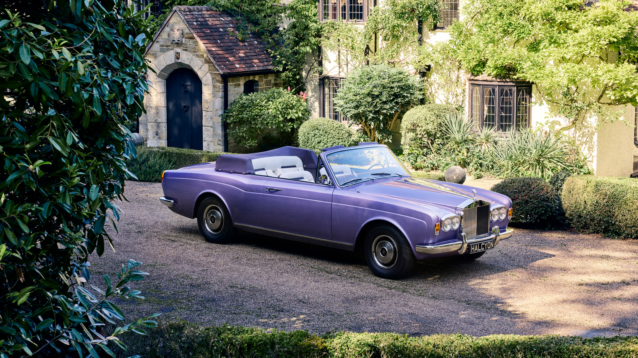 halcyon-electric-rolls-royce-corniche-front-three-quarter-cottage Front three-quarter view of the Halcyon electric Rolls-Royce Corniche parked in a garden beside an ivy-covered stone cottage.