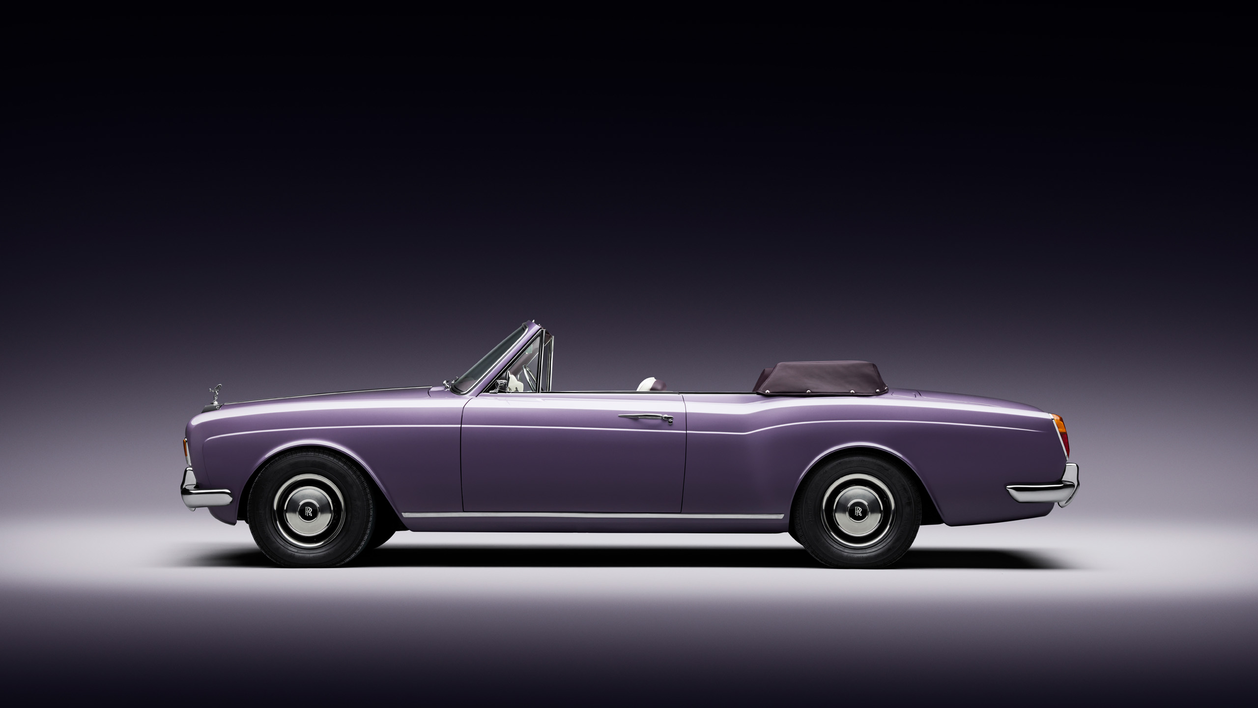 halcyon-electric-rolls-royce-corniche-side-profile A lilac Halcyon electric Rolls-Royce Corniche convertible photographed side-on in the studio, roof down, on a dark gradient background.