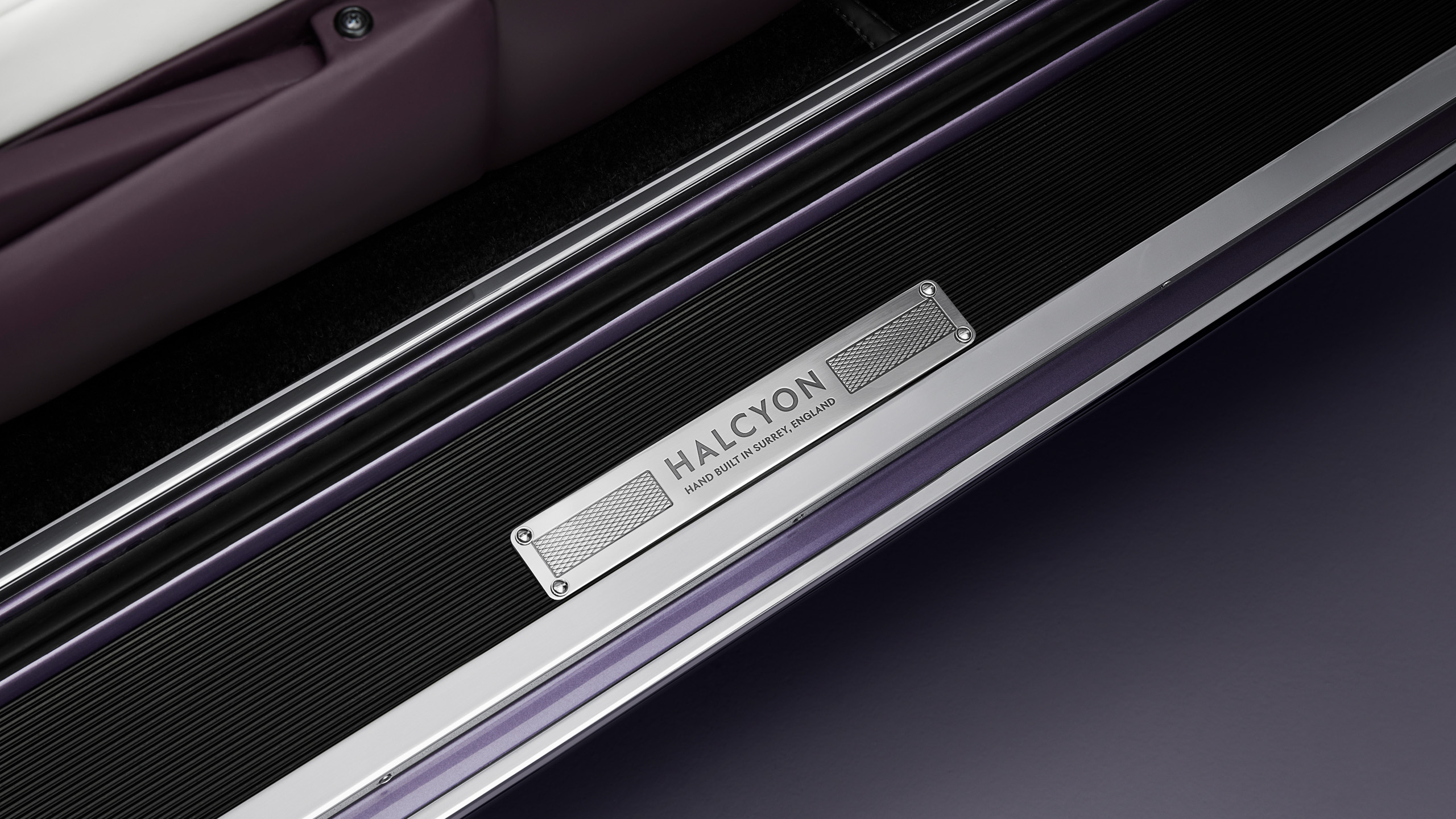 halcyon-electric-rolls-royce-corniche-sill-plate-detail Close-up of the Halcyon sill plate reading "Hand Built in Surrey, England", set against the car's aubergine and white leather interior.