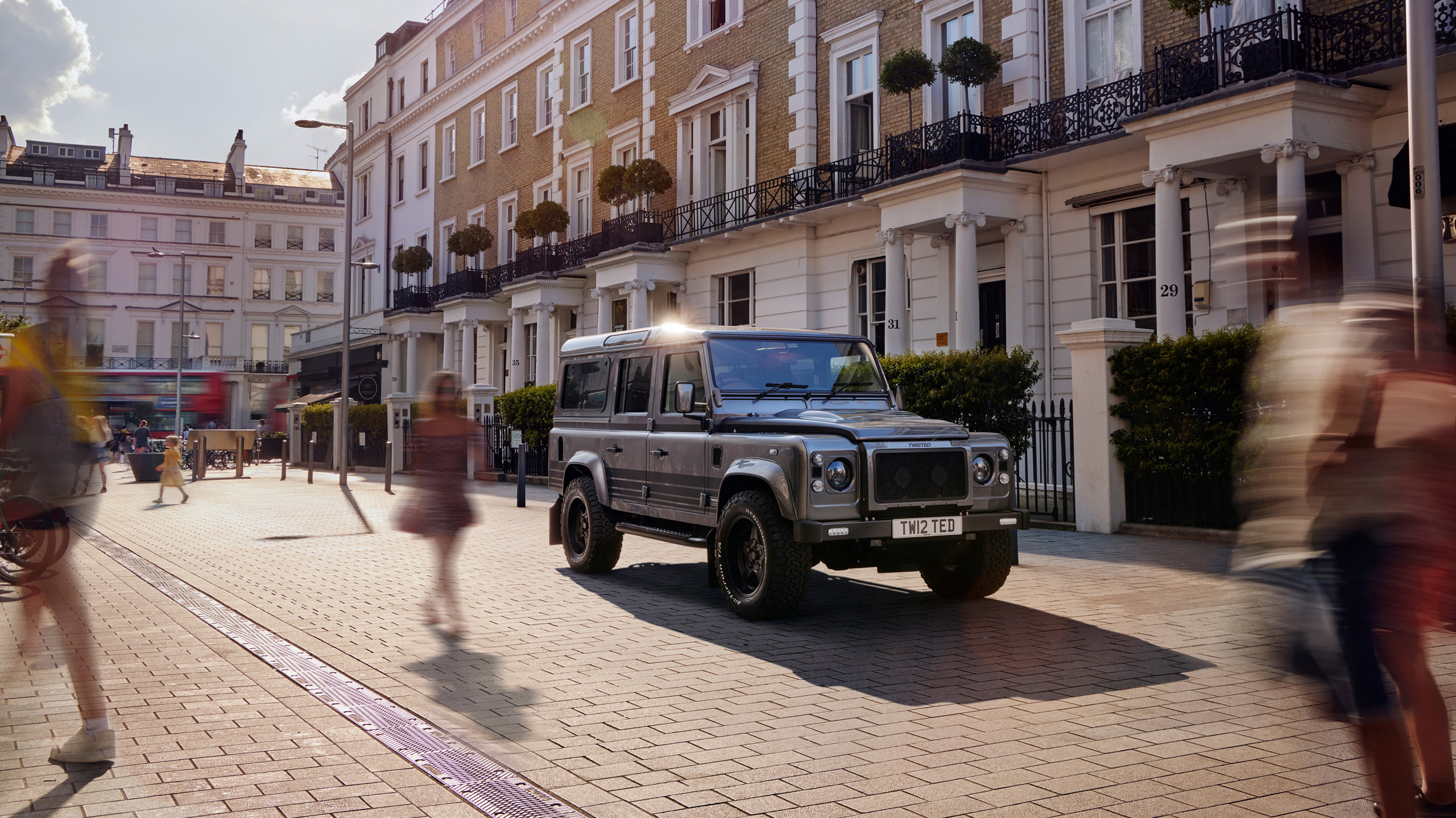 twisted-land-rover-defender-110-south-kensington-street A gunmetal Twisted Land Rover Defender 110 parked on a South Kensington street, pedestrians and a London bus passing by.