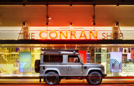 Square-format shot of a silver Twisted Land Rover Defender 90 parked outside The Conran Shop in London at night.