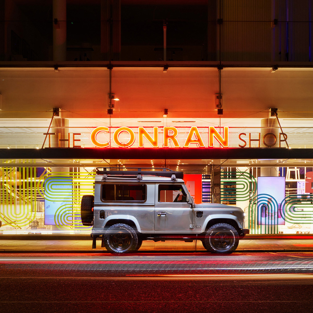 Square-format shot of a silver Twisted Land Rover Defender 90 parked outside The Conran Shop in London at night.