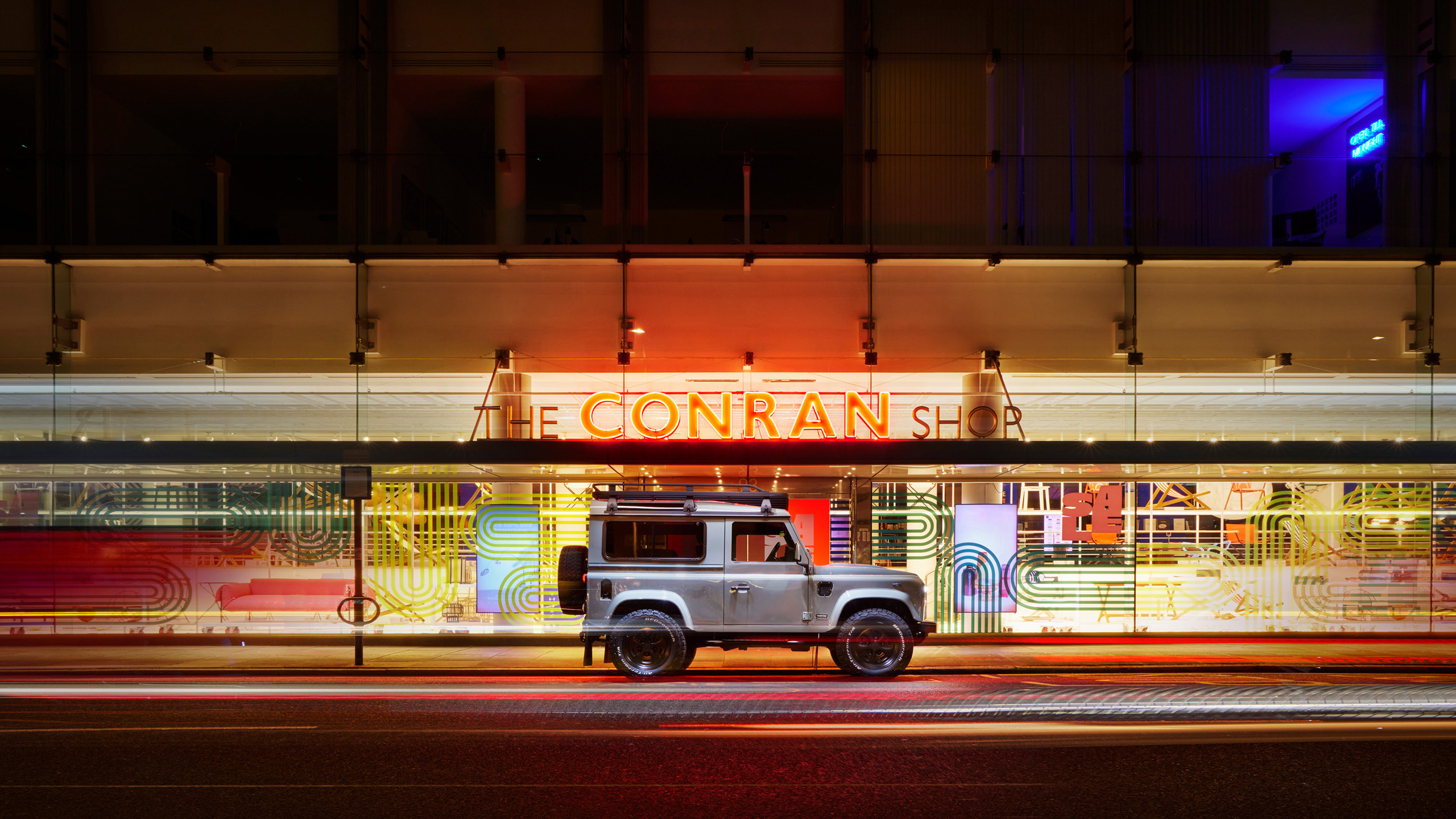twisted-land-rover-defender-conran-shop-night A silver Twisted Land Rover Defender 90 parked outside The Conran Shop in London at night, neon signage lit above.