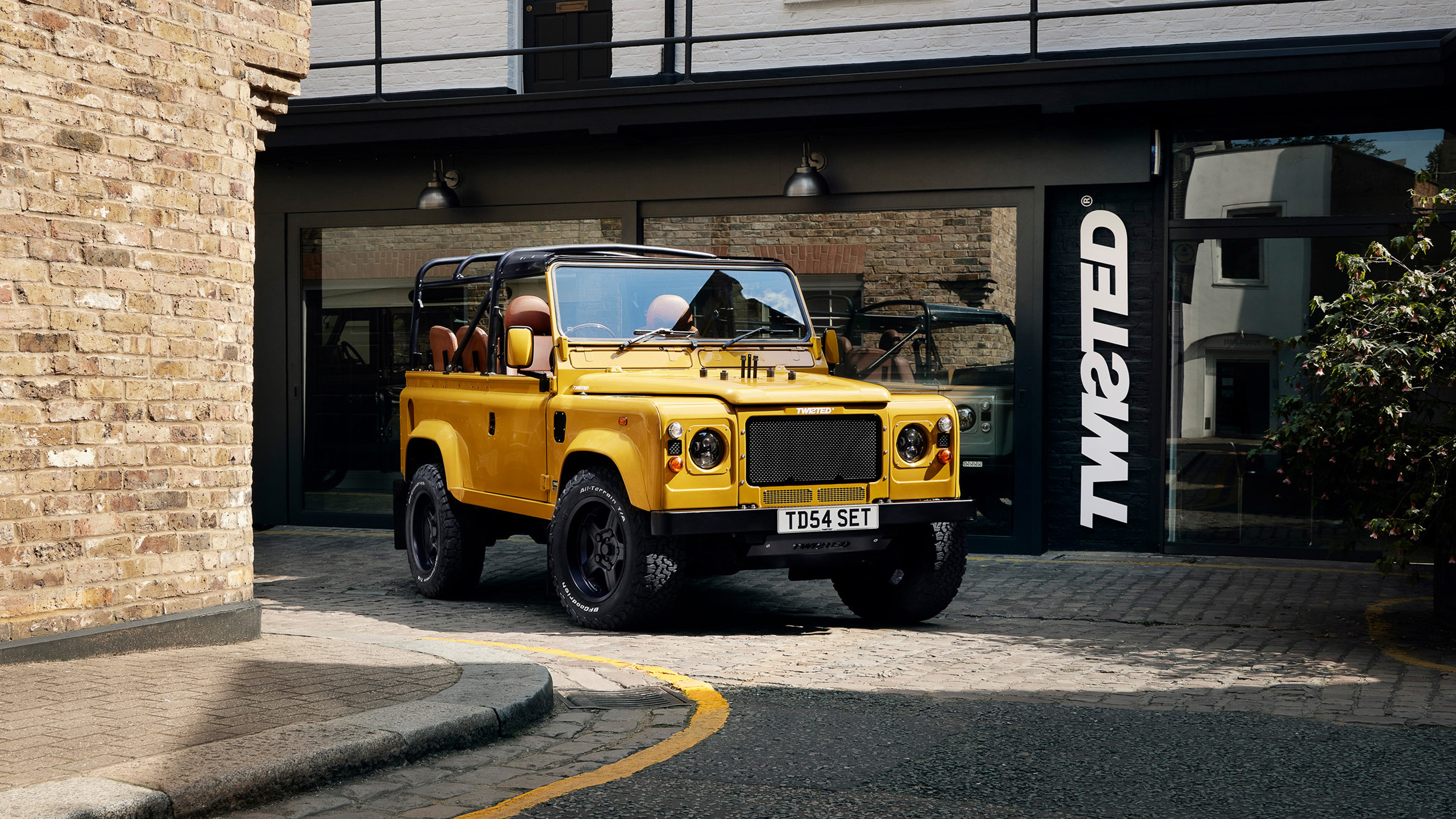 twisted-land-rover-defender-yellow-mews-side A yellow Twisted Land Rover Defender pickup parked in a London mews, Twisted signage visible on the building behind.